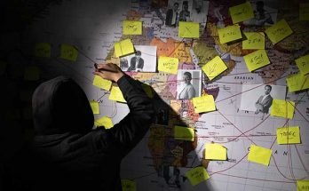 A person in a black hoodie with photos and post-its linked together with red string