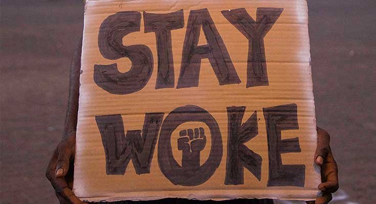 Man holding a cardboard sign that says "Stay Woke"